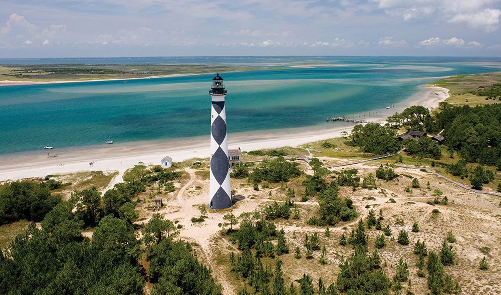 Cape Lookout Lighthouse in North Carolina, black and white diamond pattern, on a sandy island with ocean and marsh in the background.