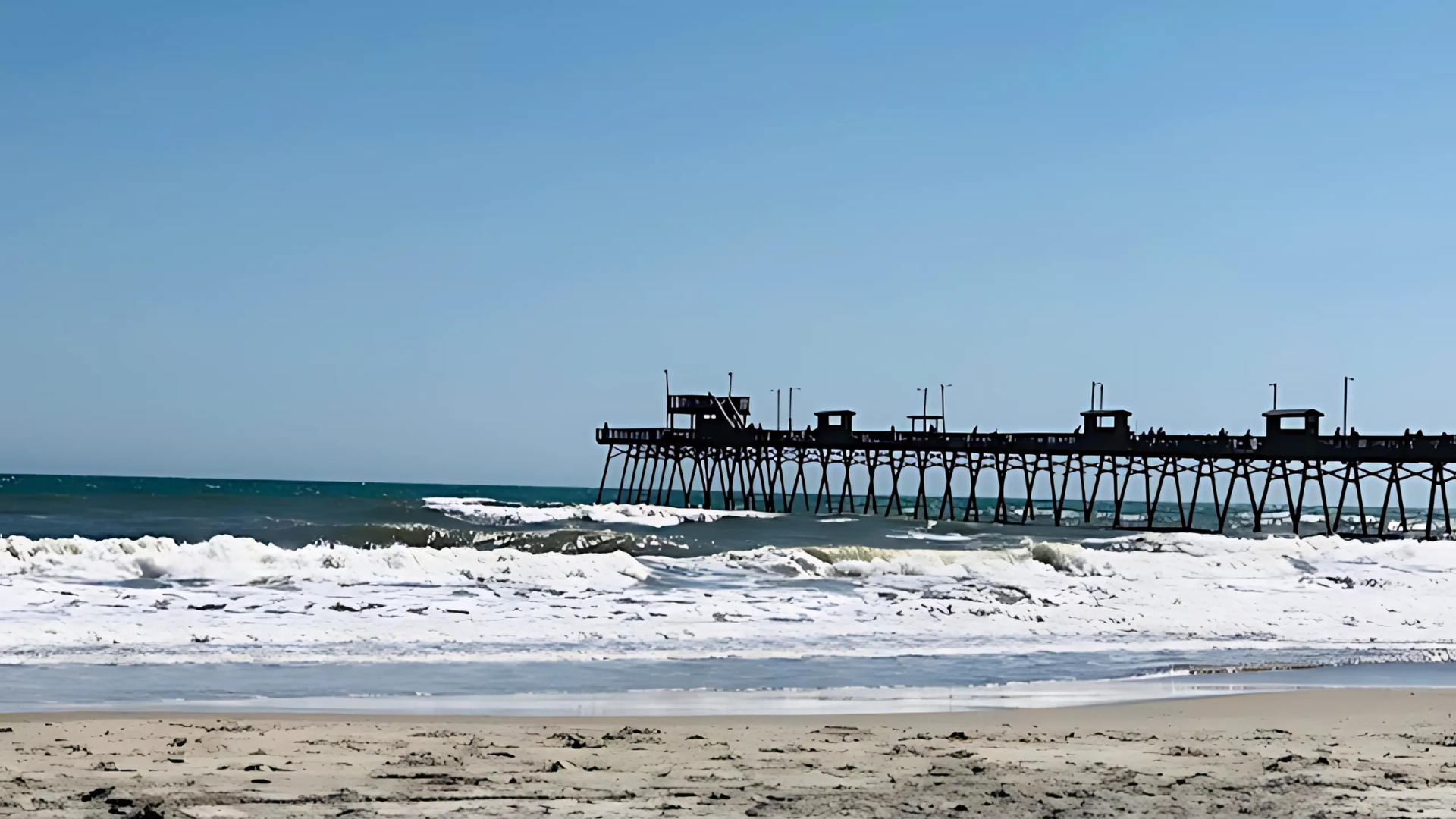 Waterfront with docks, buildings, and reflections under a clear blue sky.