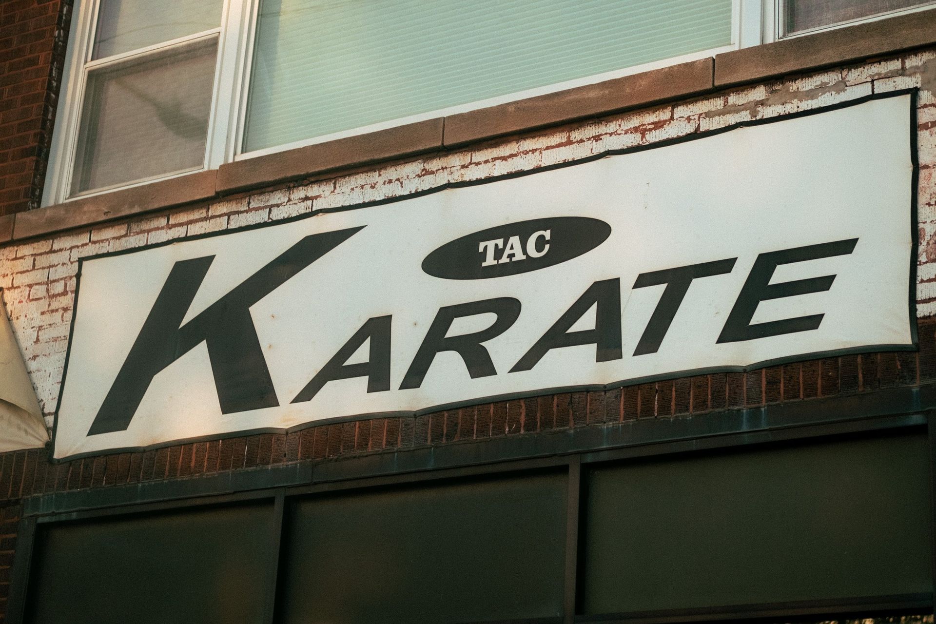 A sign for tac karate hangs on a brick building