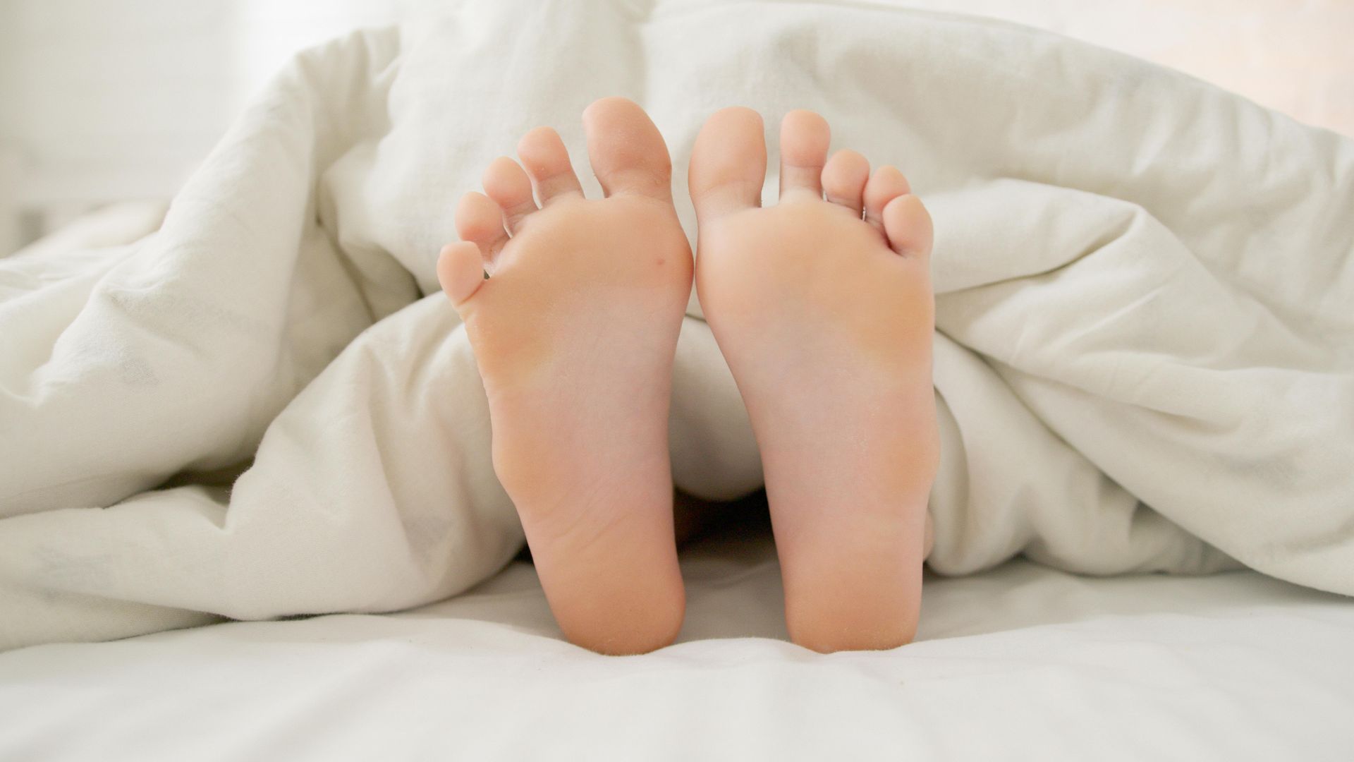 A person 's feet sticking out of a white blanket on a bed.