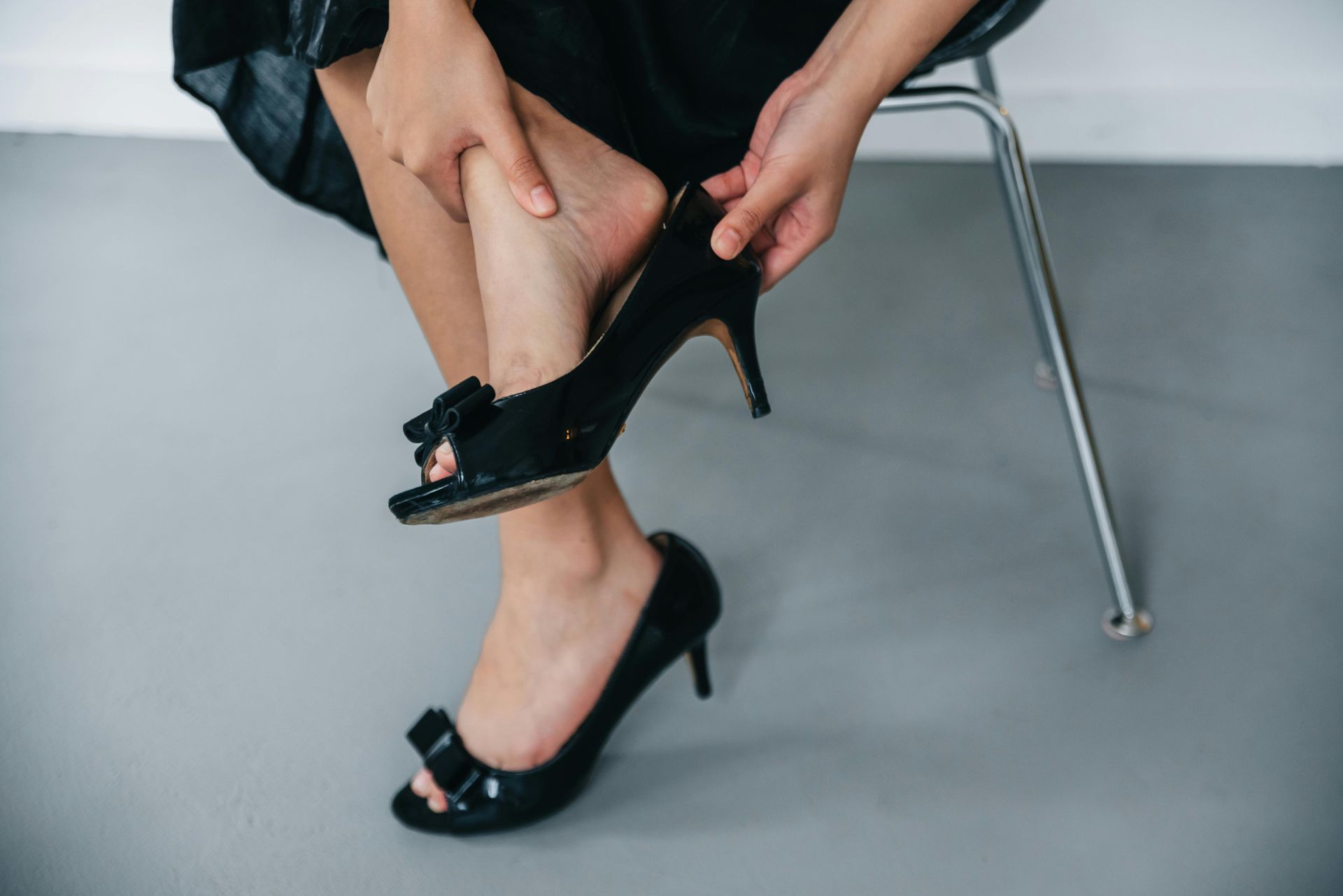 A woman is sitting on a chair putting on a pair of black high heels.