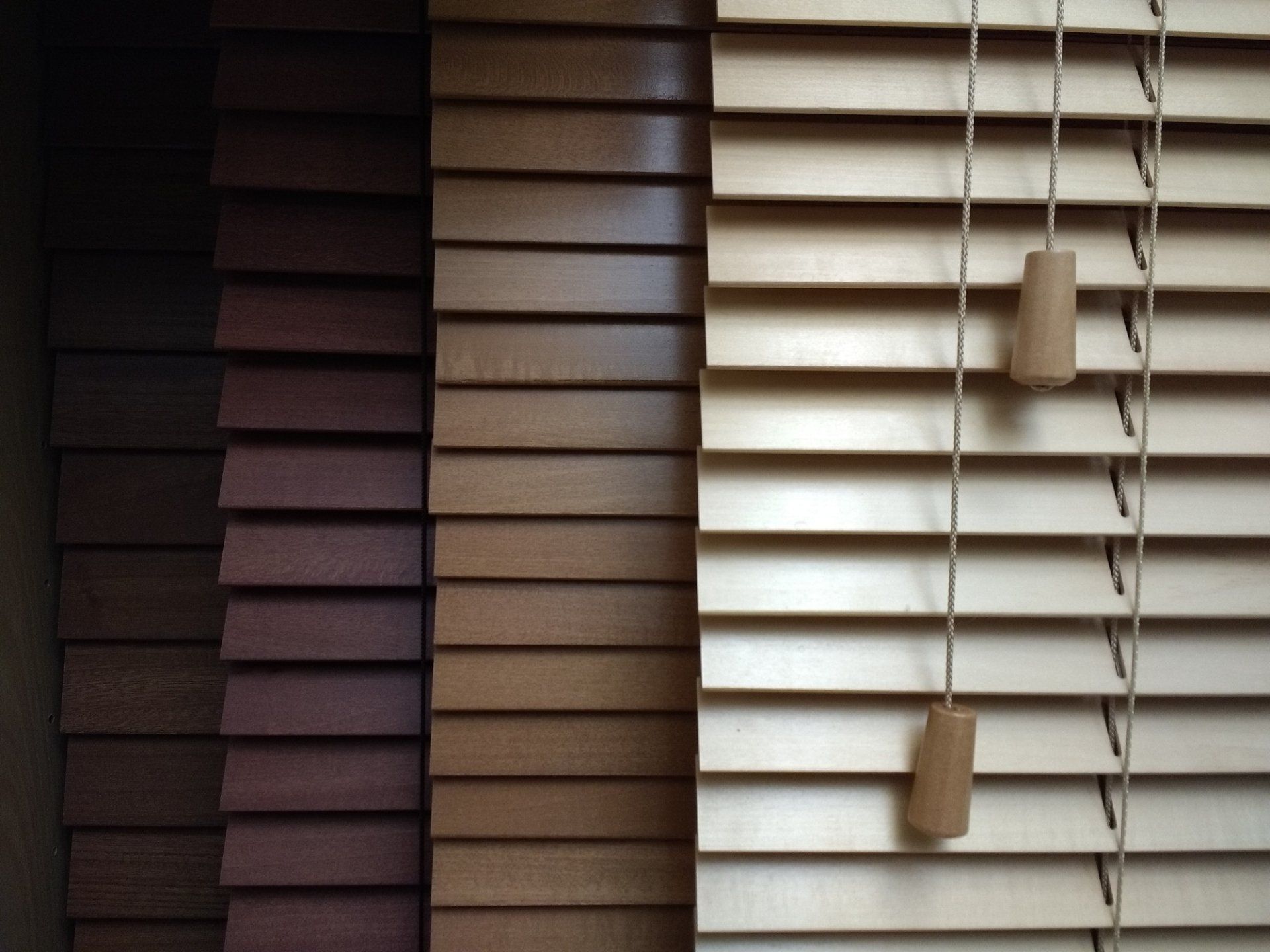 Wooden blinds in various shades of brown, with pull cords.