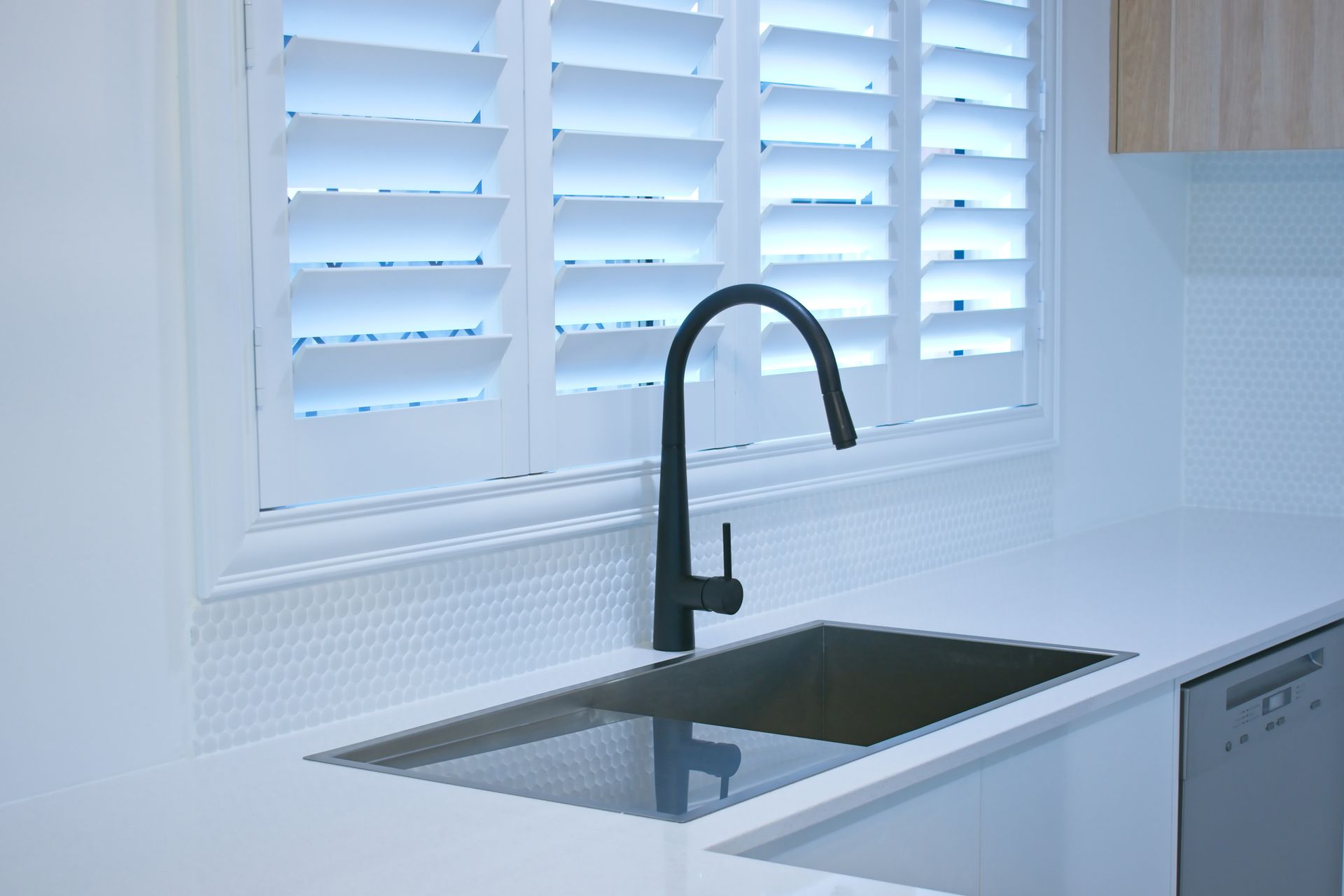 Close-up of a black kitchen sink in a white room, in front of a pair of white plantation shutters. Close-up of a black kitchen sink in a white room, in front of a pair of white plantation shutters.