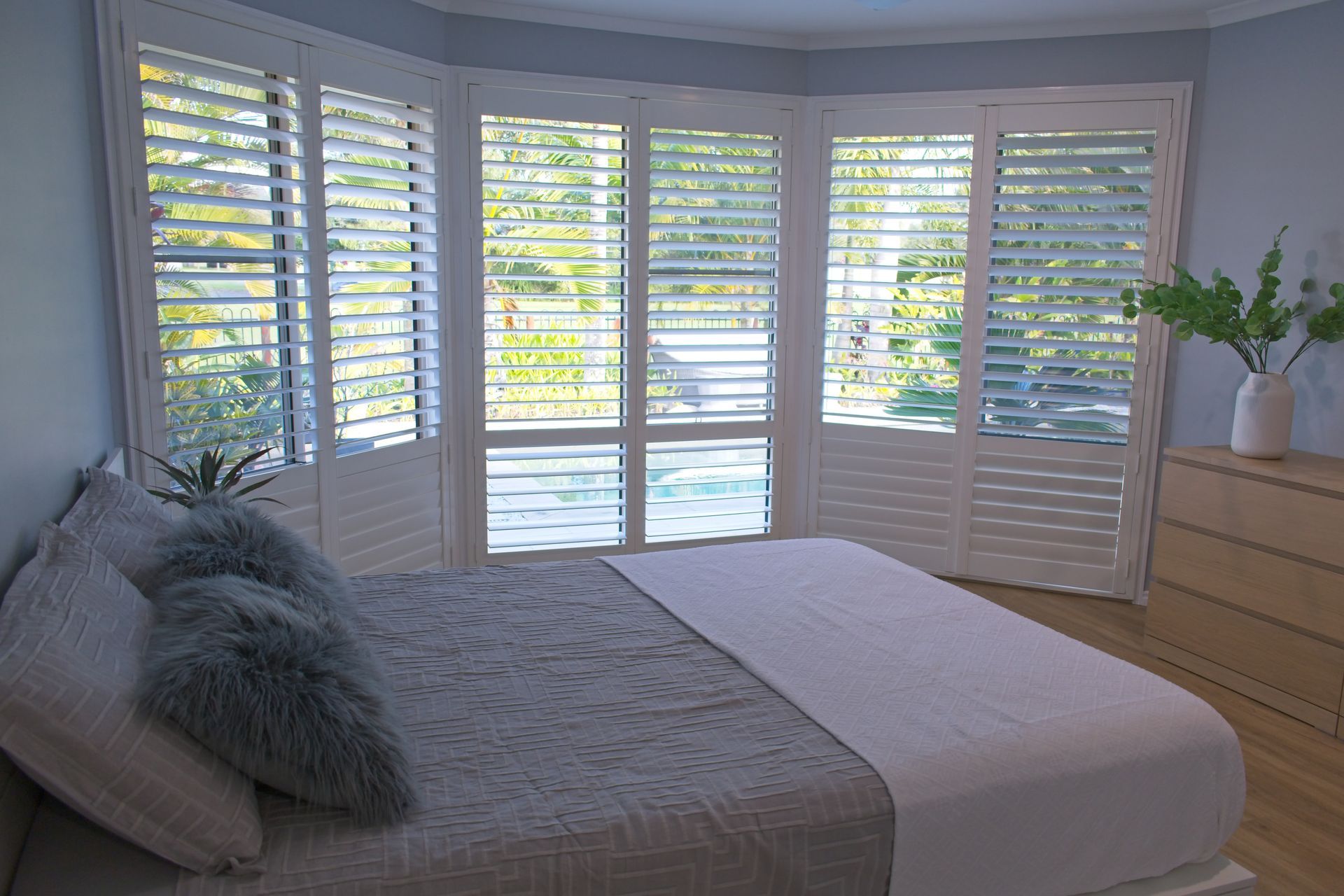 White luxury plantation shutters and a grey bed in a bedroom with blue walls.