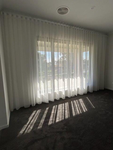 White sheer curtains frame a window, casting shadows across a dark carpeted room.