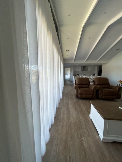 Sheer white curtains in a modern living room with brown recliner chairs and a kitchen in the background.