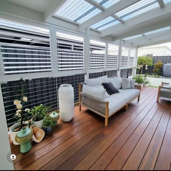 Outdoor lounge area with wooden deck, white sofa, shutters, and potted plants.
