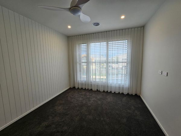 Empty room with dark carpet, window with sheer curtains, ceiling fan, and light-colored walls.