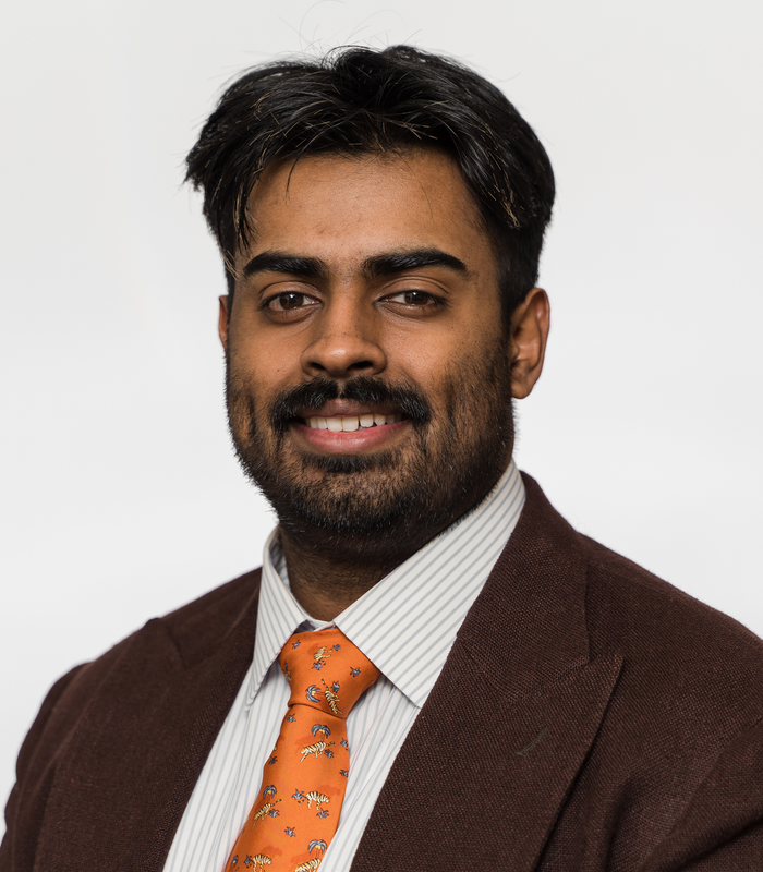 A man with a beard wearing an orange tie and a brown jacket