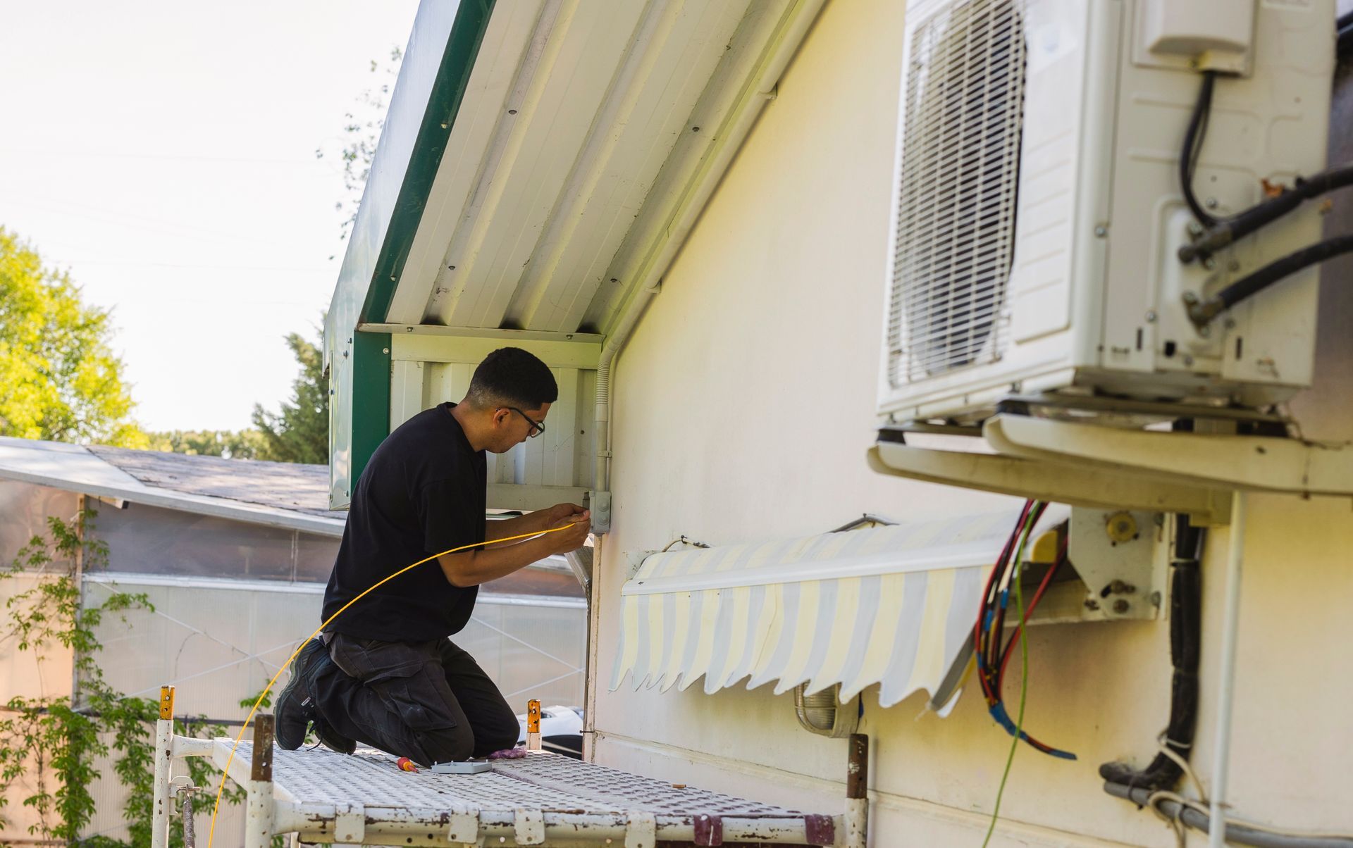 Man installing electrical wiring on the exterior of a building next to an AC unit.