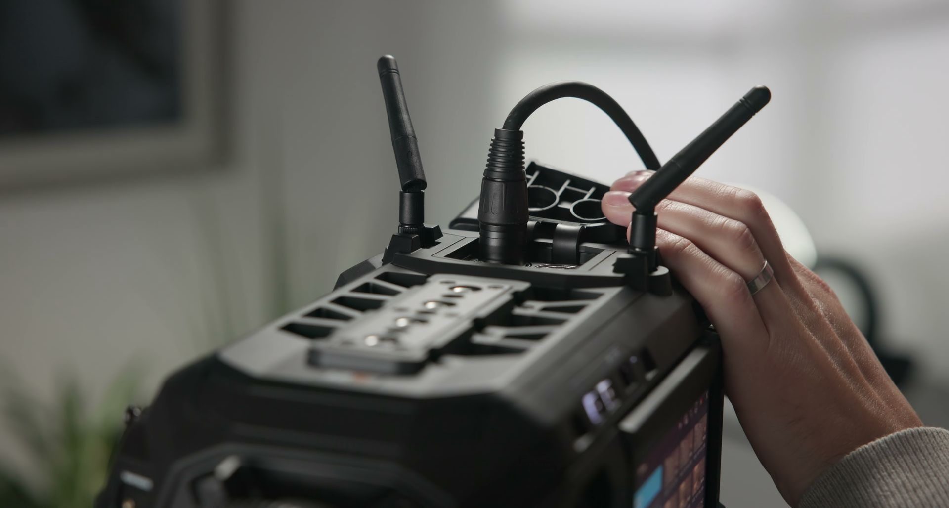 Person's hand adjusting antennas on a black device, likely video equipment, indoors.
