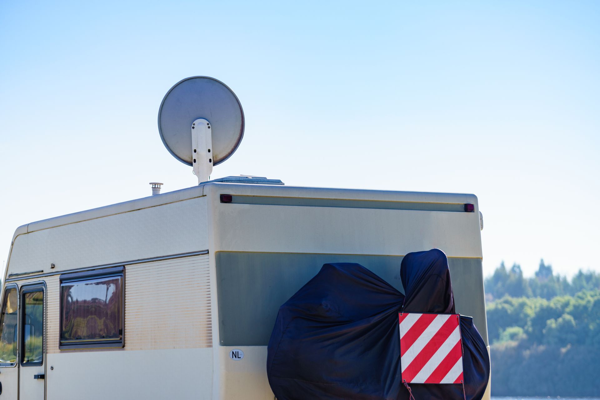 Camper van with satellite dish, spare tire cover, and hazard marker on a sunny day.