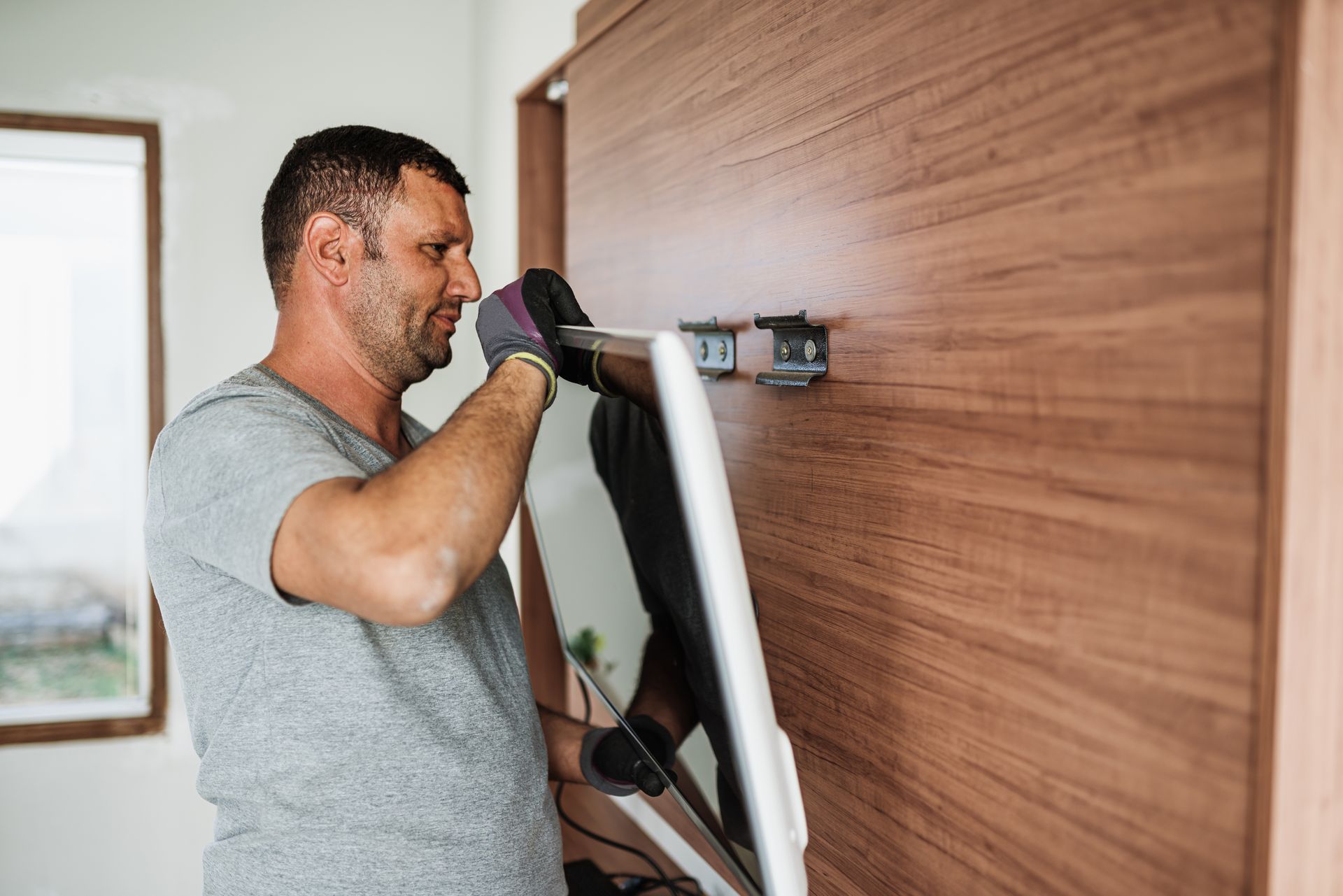 Man wearing gloves attaching a TV to a wooden wall.