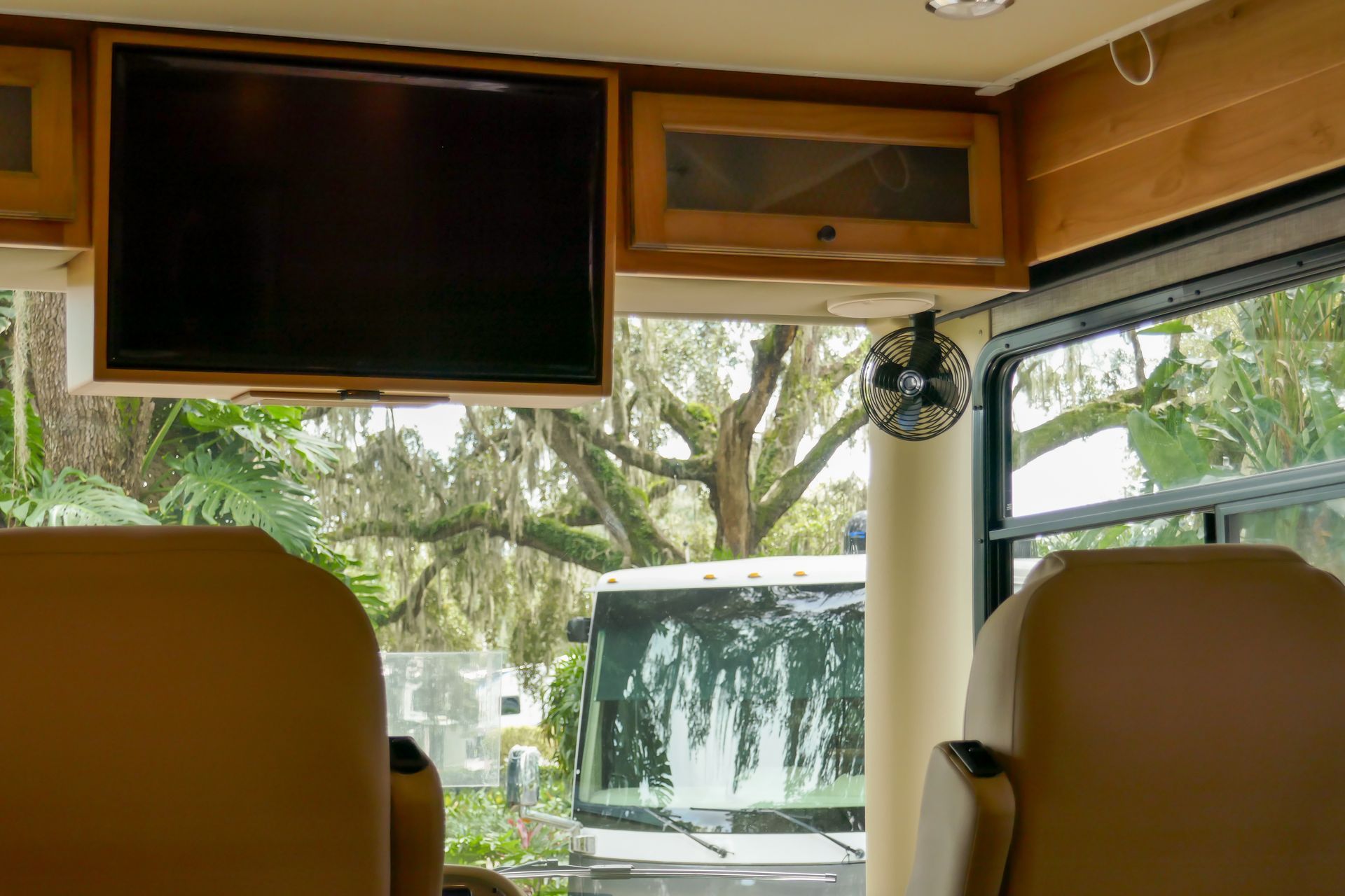 Interior of RV with TV, cabinets, and a window looking out at a tree and part of another vehicle.