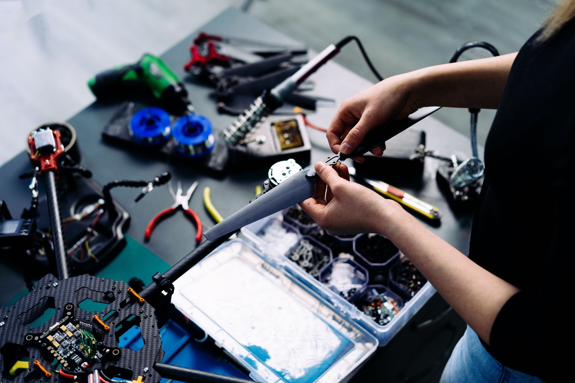 Person working on electronics, surrounded by tools and parts on a table.