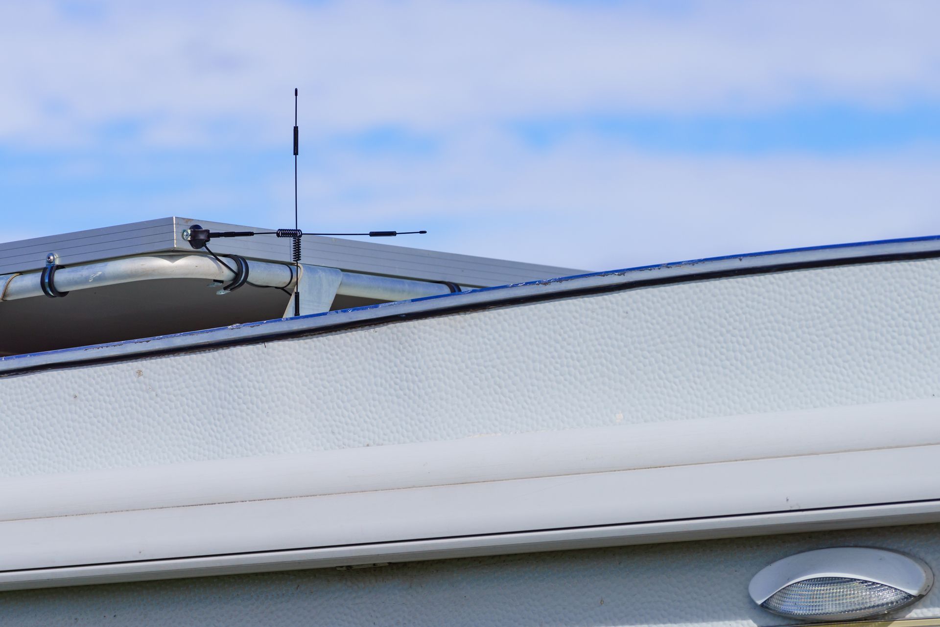 White RV with antenna on roof against a blue and cloudy sky.