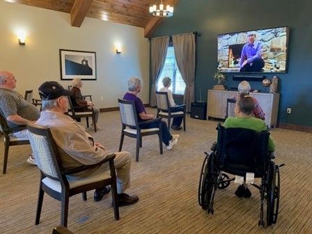 A group of elderly people are sitting in chairs and watching a television.