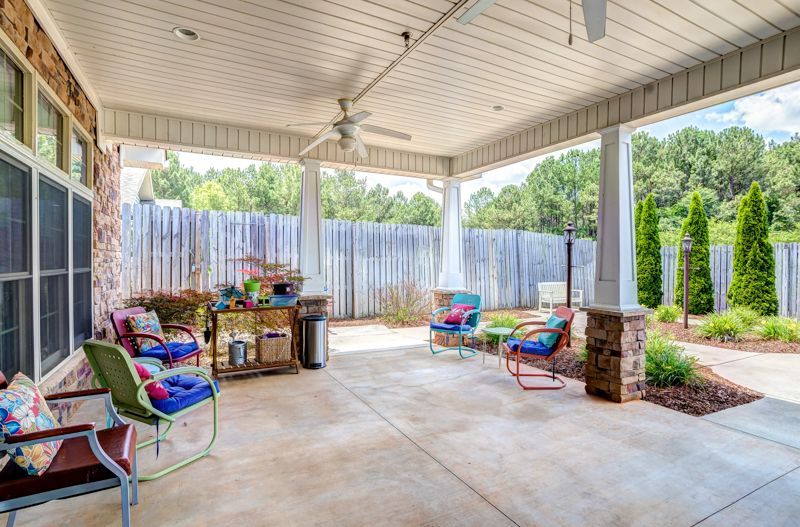 A large covered patio with chairs , a table and a ceiling fan.