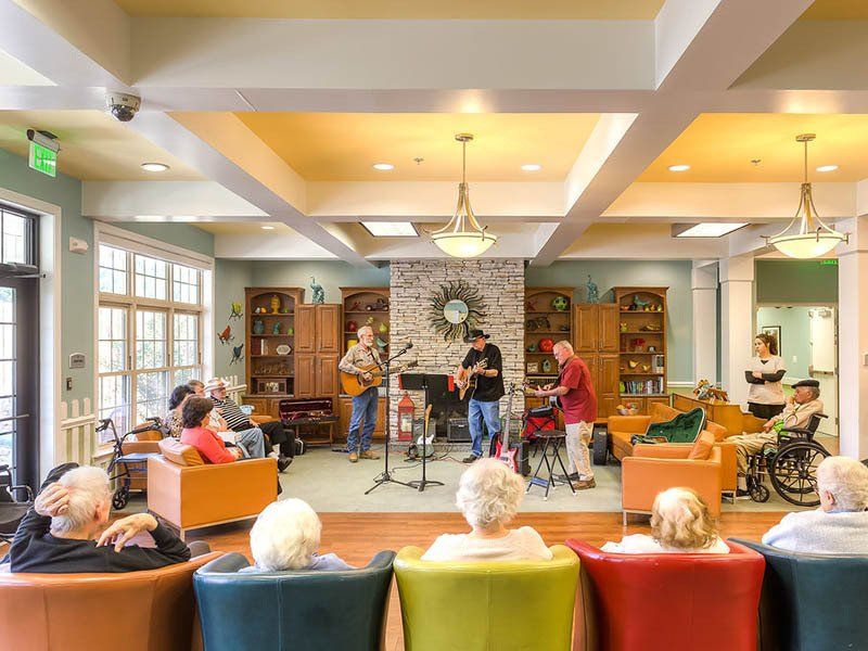 A group of people are sitting in chairs in a living room watching a band play music.