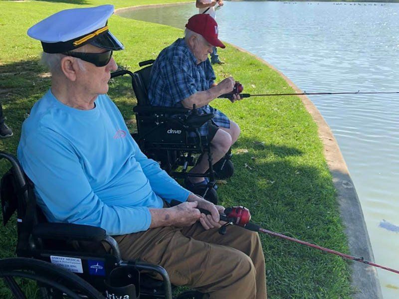 A man in a wheelchair is fishing on the shore of a lake.