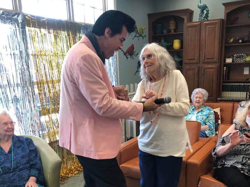 A man in a pink jacket is holding a microphone in front of an elderly woman.