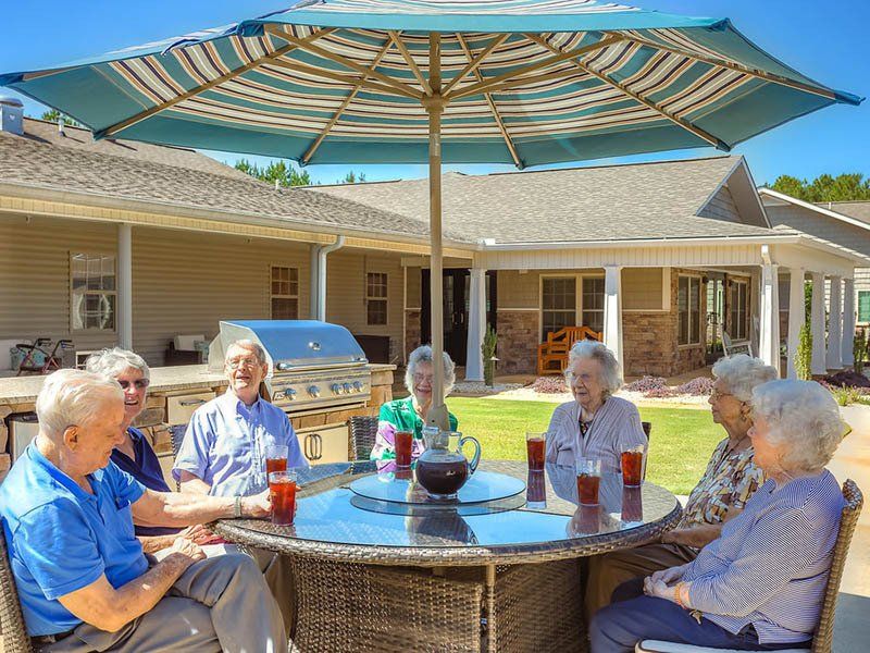 A group of elderly people are sitting around a table under an umbrella.