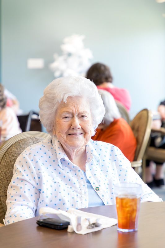 An elderly woman is sitting at a table with a glass of iced tea.