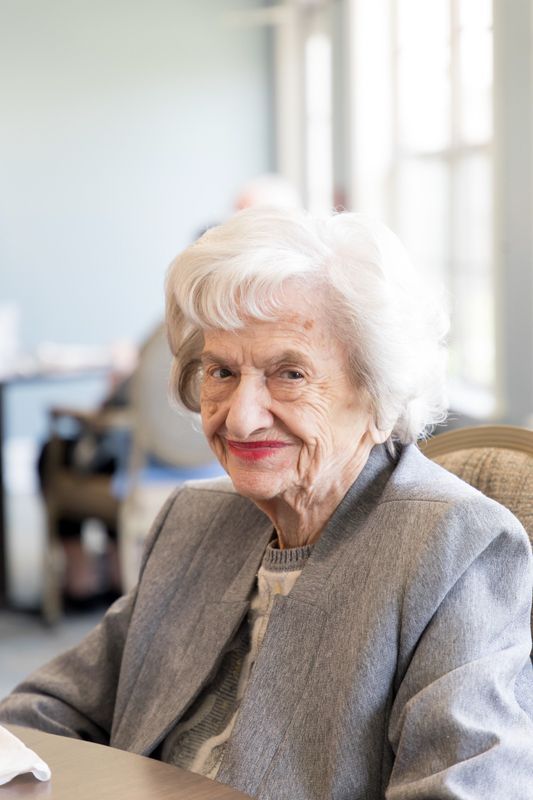 An elderly woman is sitting at a table and smiling at the camera.