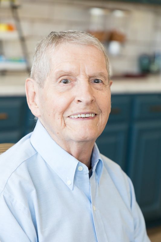 An elderly man in a blue shirt is smiling for the camera.