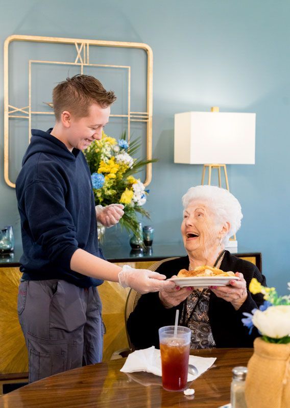 A young man is serving food to an older woman at a table.