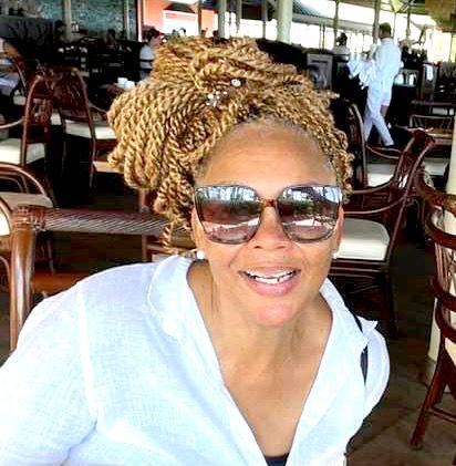 A woman wearing sunglasses and braids is sitting at a table in a restaurant.