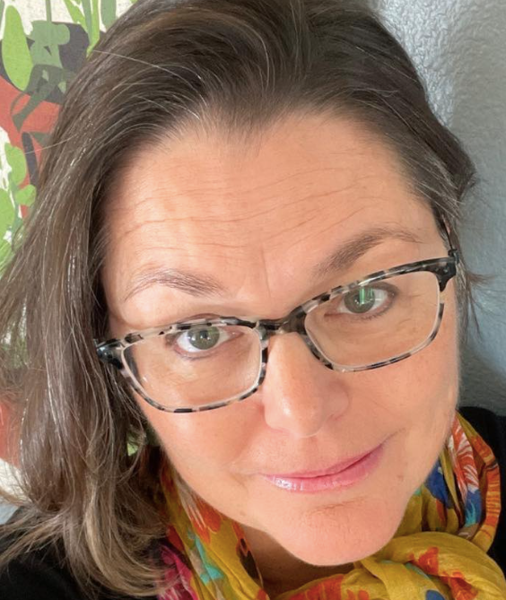 A woman wearing glasses and a scarf is smiling for the camera. Beki Buell life coach, life coach training, the coaching guild