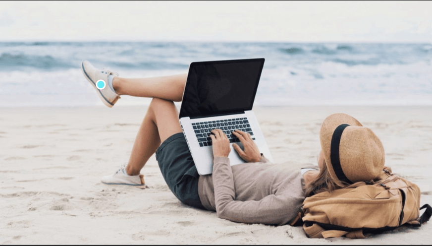 A woman is laying on the beach using a laptop computer. Living the life coaching dream