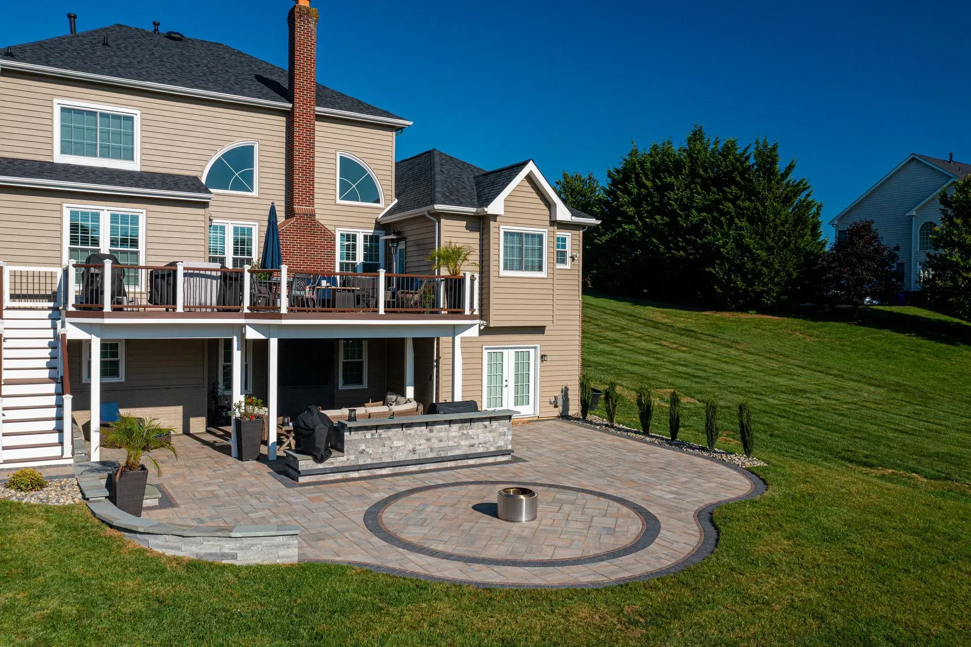 Backyard with multi-level deck, stone patio with fire pit, and sloped lawn on a sunny day.