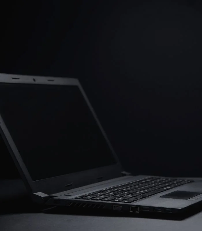 Laptop with black screen on dark background.