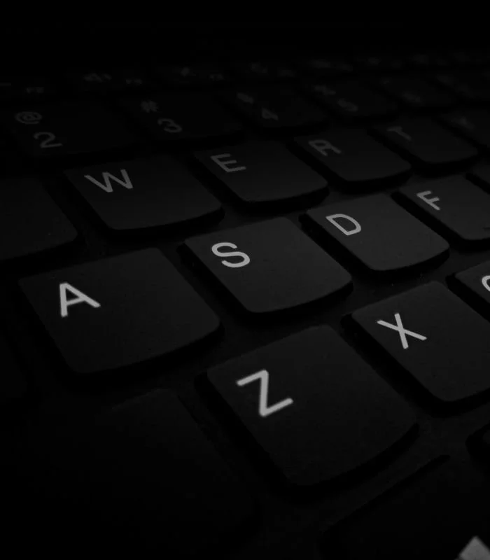 Close-up of a black laptop keyboard, letters lit white against the dark keys.
