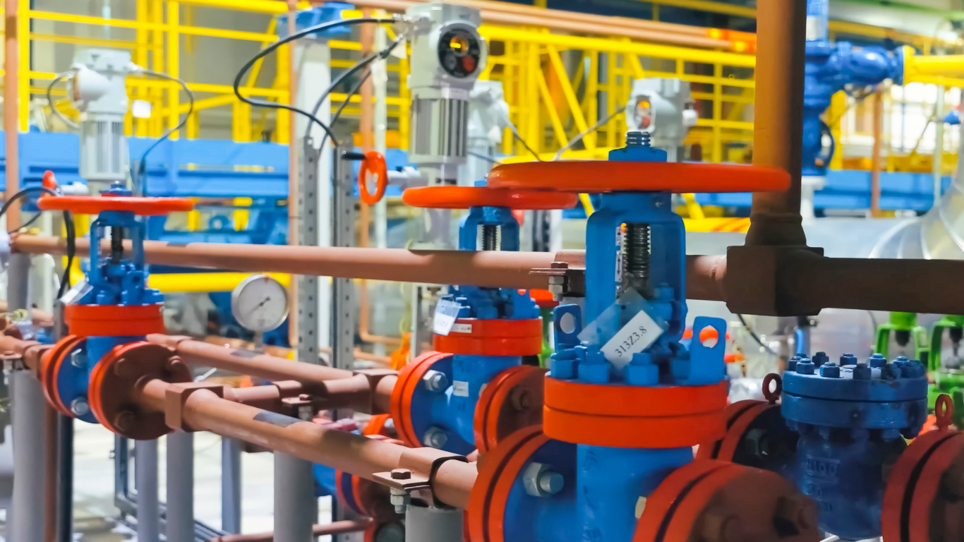 Blue and orange industrial valves on brown pipes in a factory setting.