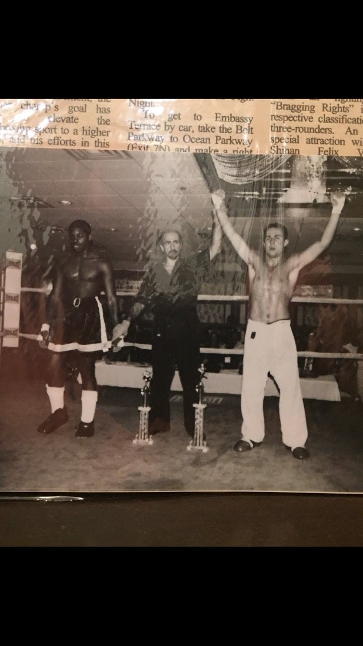 Boxers with trophies in a ring; one raises arms in victory. Black and white photo.