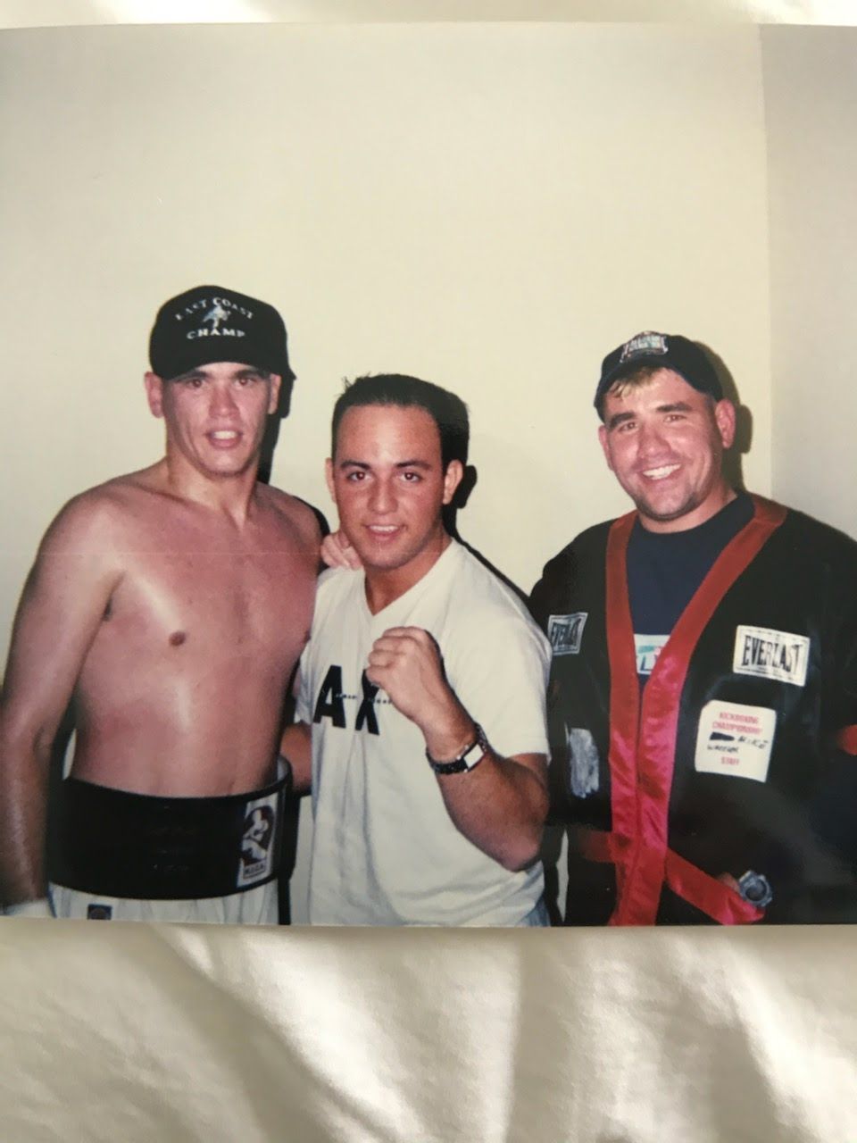 Three men posing for a photo. Boxer in trunks, center man clenches fist, man in corner has a robe on.
