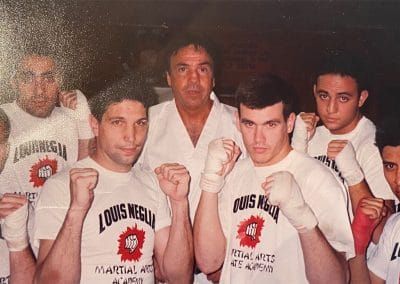 Group photo of men in boxing gear, some with fists raised, in front of a man in a white gi.
