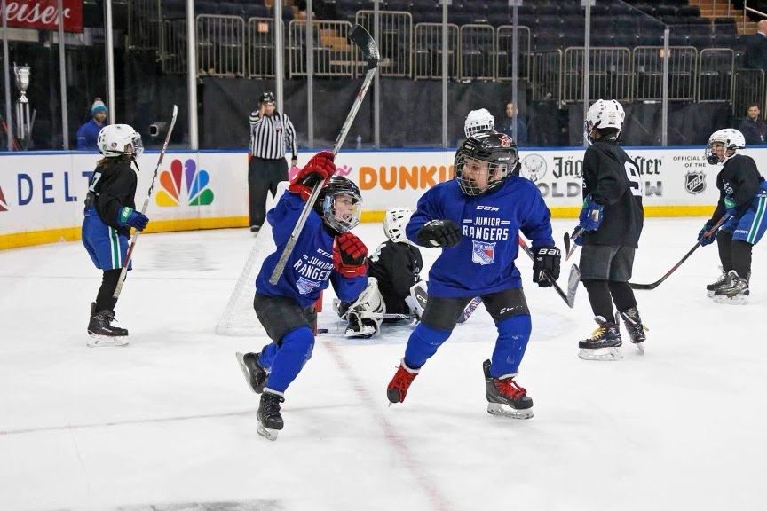 Young hockey players in blue jerseys celebrating a goal on an ice rink.