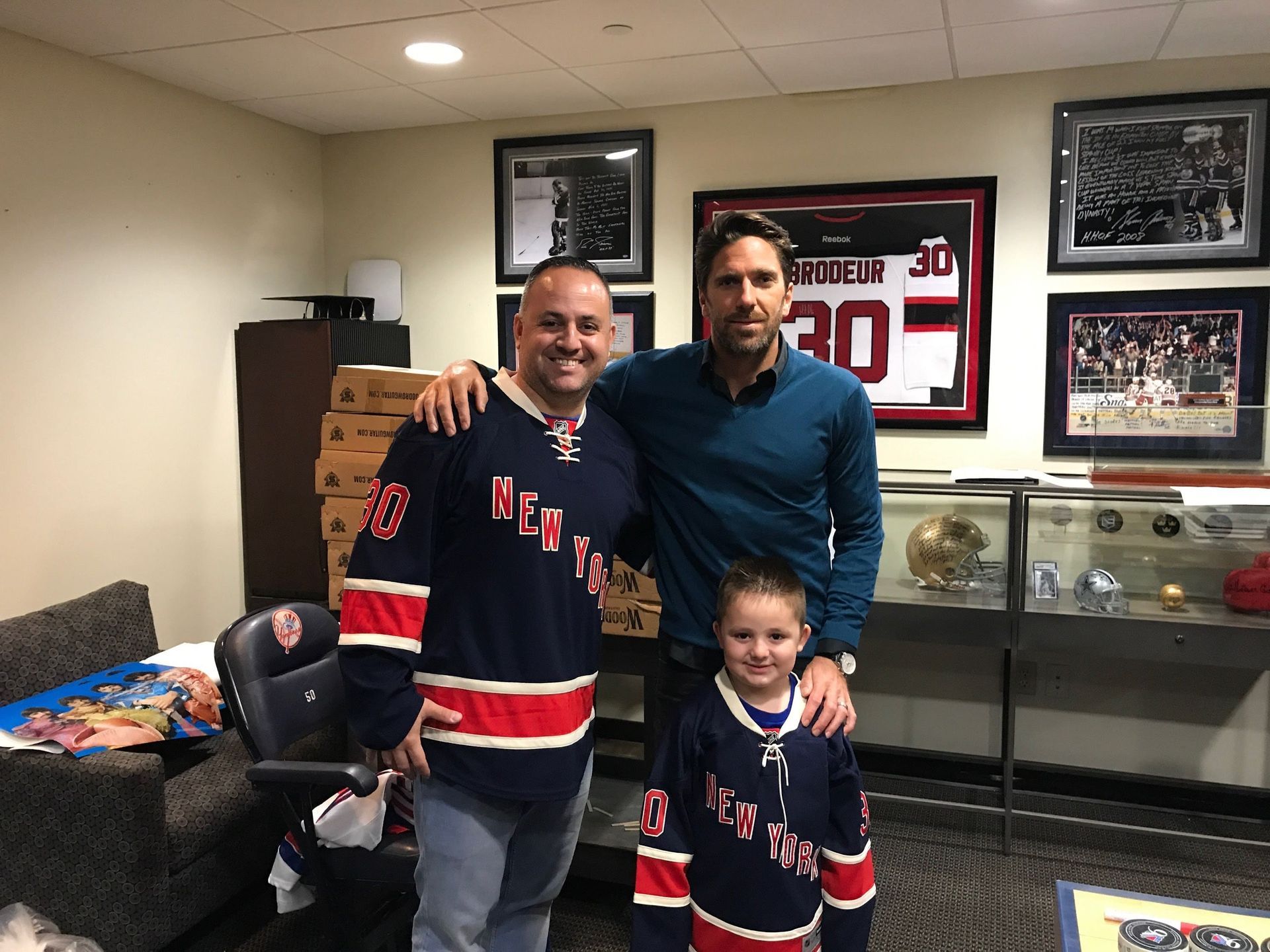 Three people pose for a photo: two men and a young girl. All wear New York Rangers jerseys indoors.