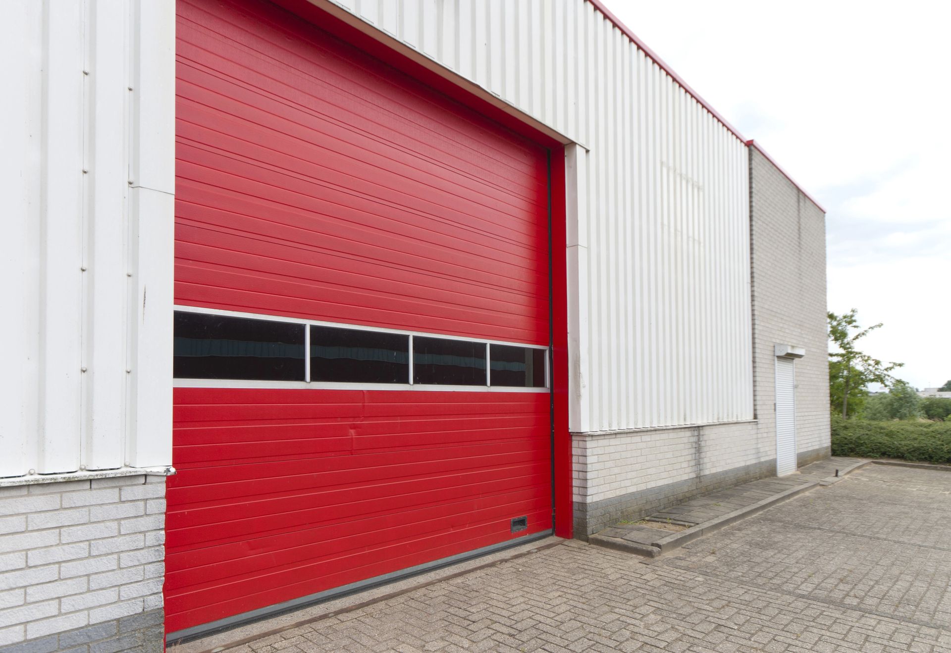 Red industrial loading bay door on a white warehouse exterior
