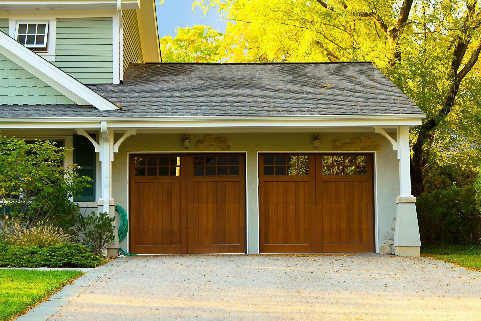 Wooden double garage doors beneath a shingled roof on a suburban house
