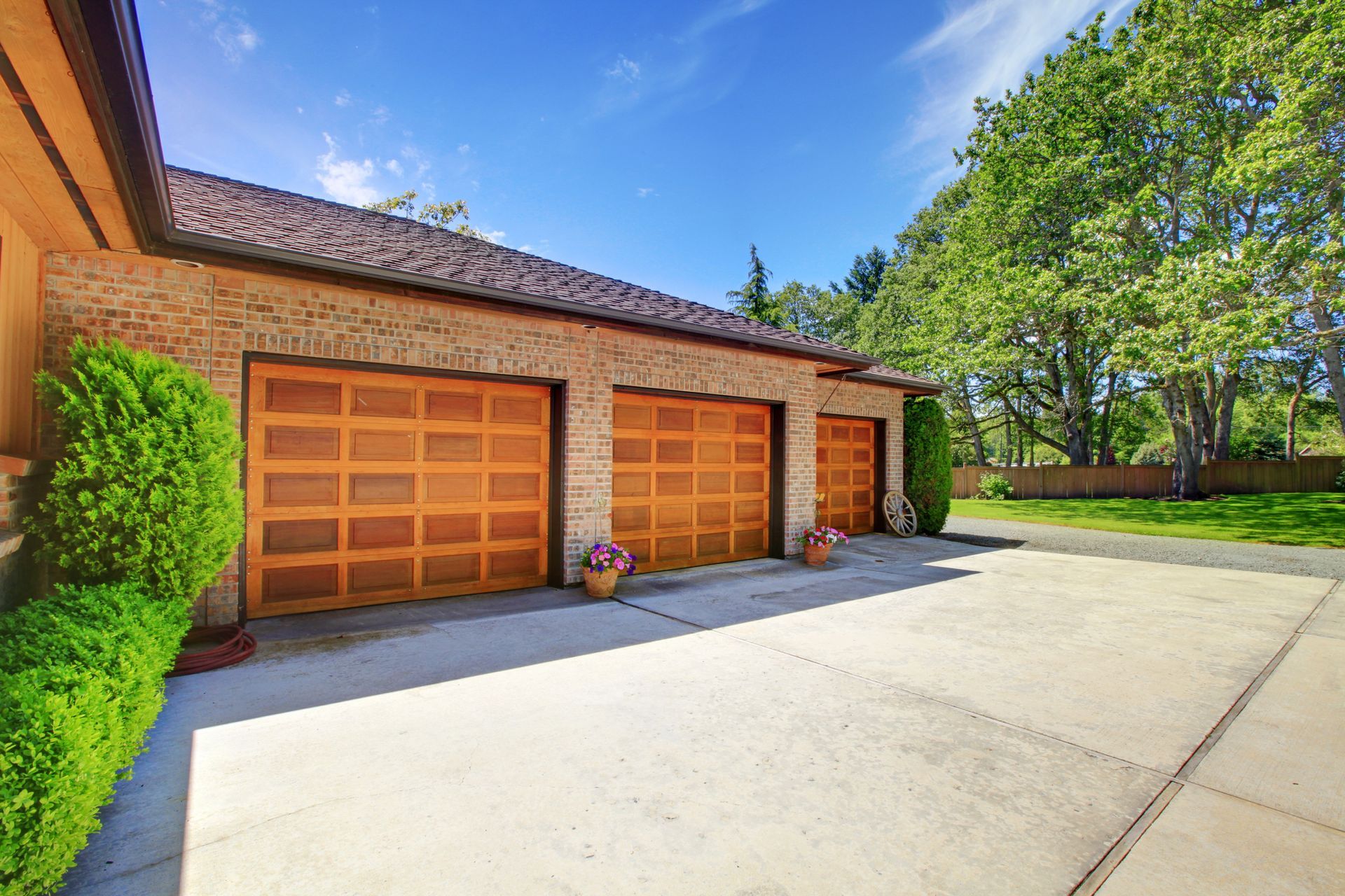 Brick house with two wooden garage doors and a wide concrete driveway under a bright blue sky