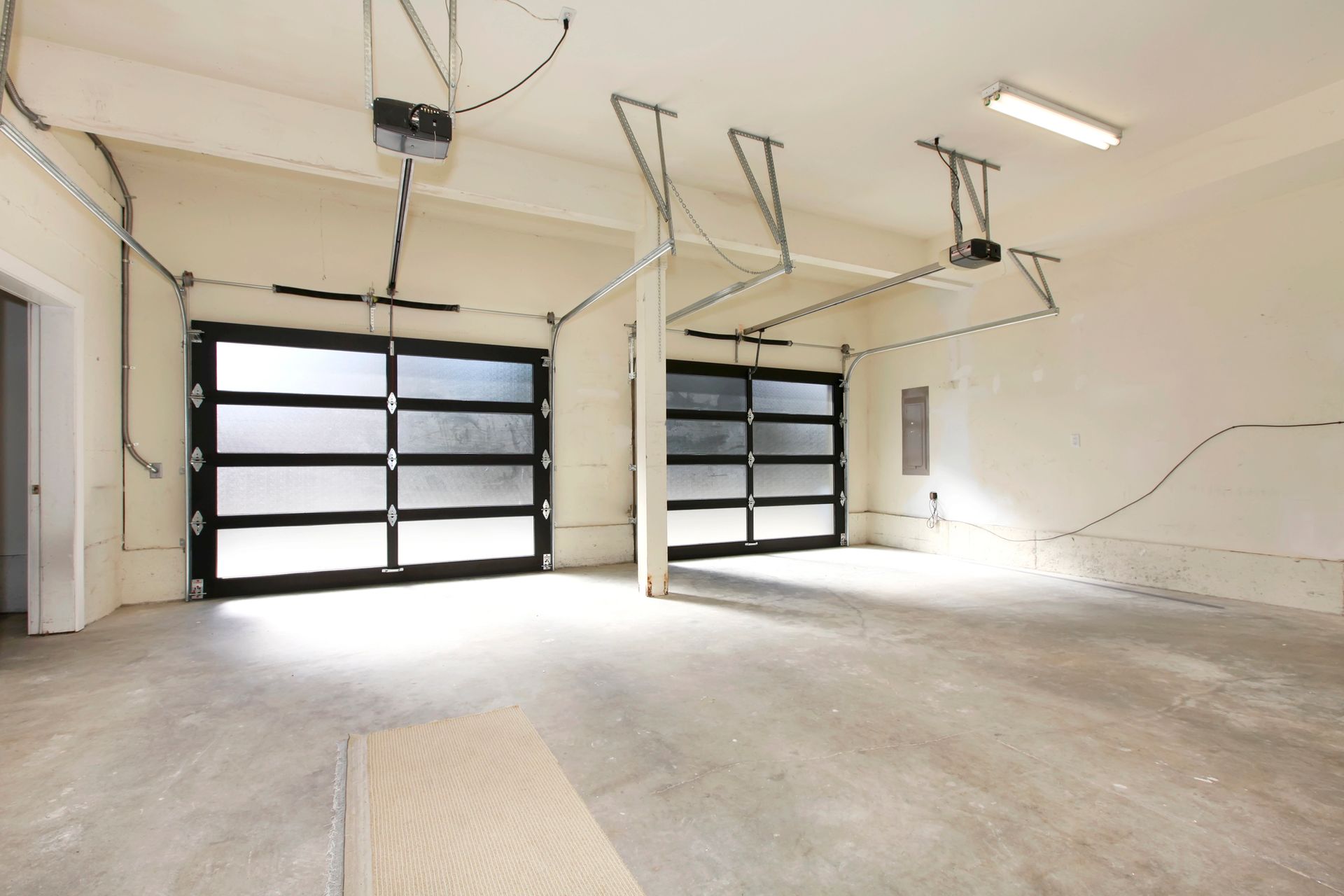 Empty white garage with two black overhead doors and exposed ceiling tracks