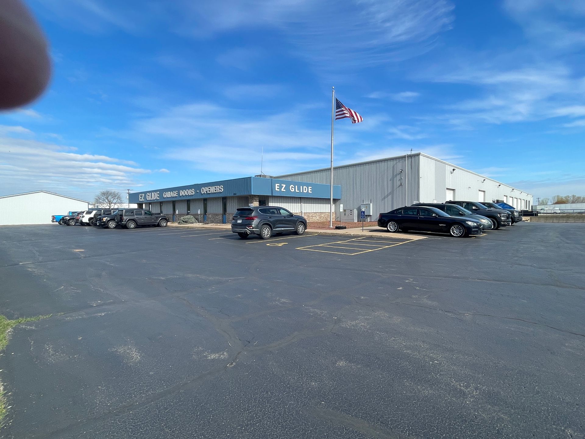 Industrial building with parked cars and an American flag flying under a blue sky