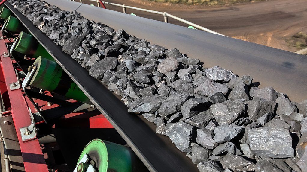 Conveyor belt transporting a pile of dark gray coal chunks at an outdoor mining site.
