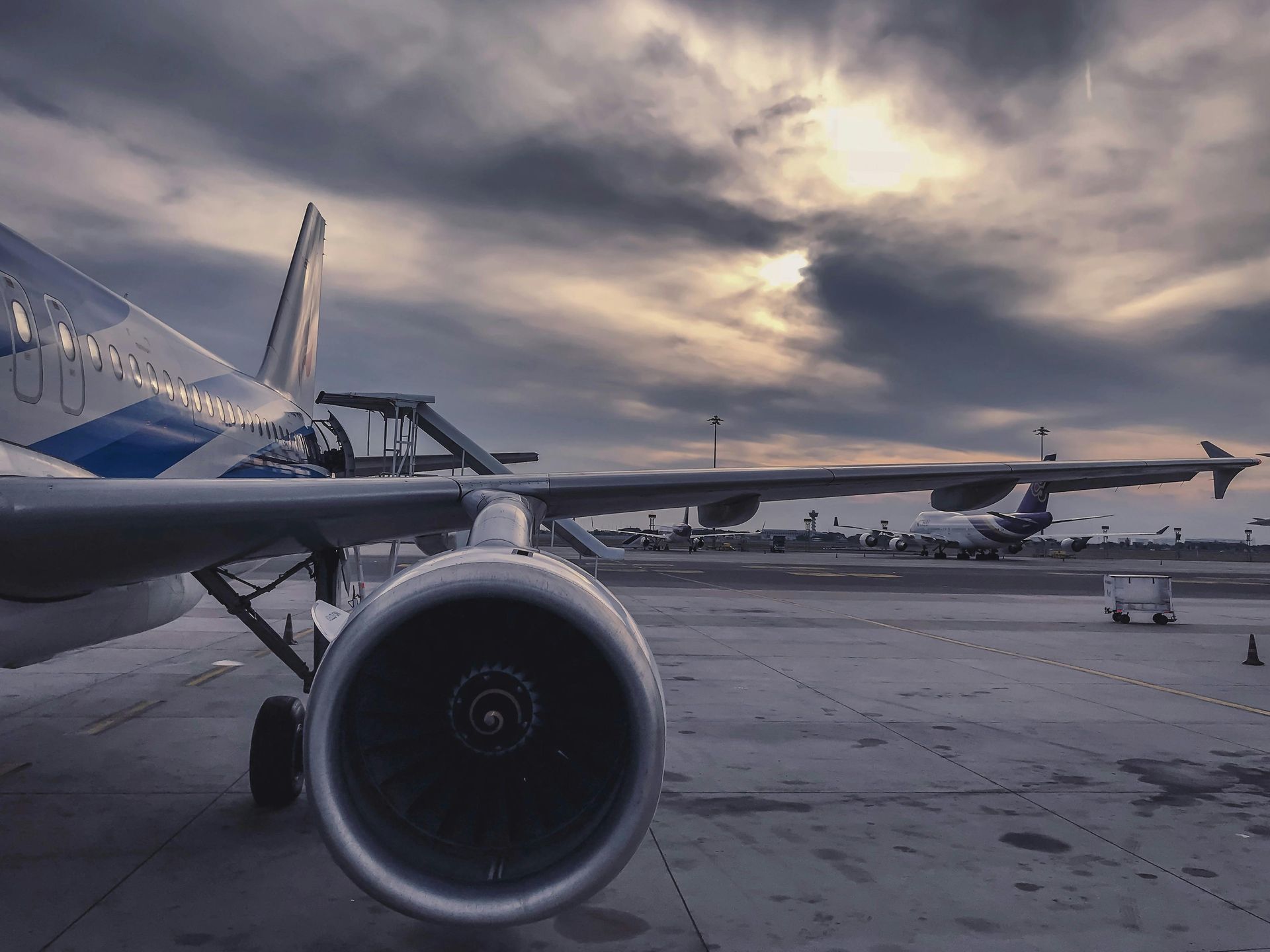 Airplane parked on tarmac under a cloudy sky. Jet engine is prominent.