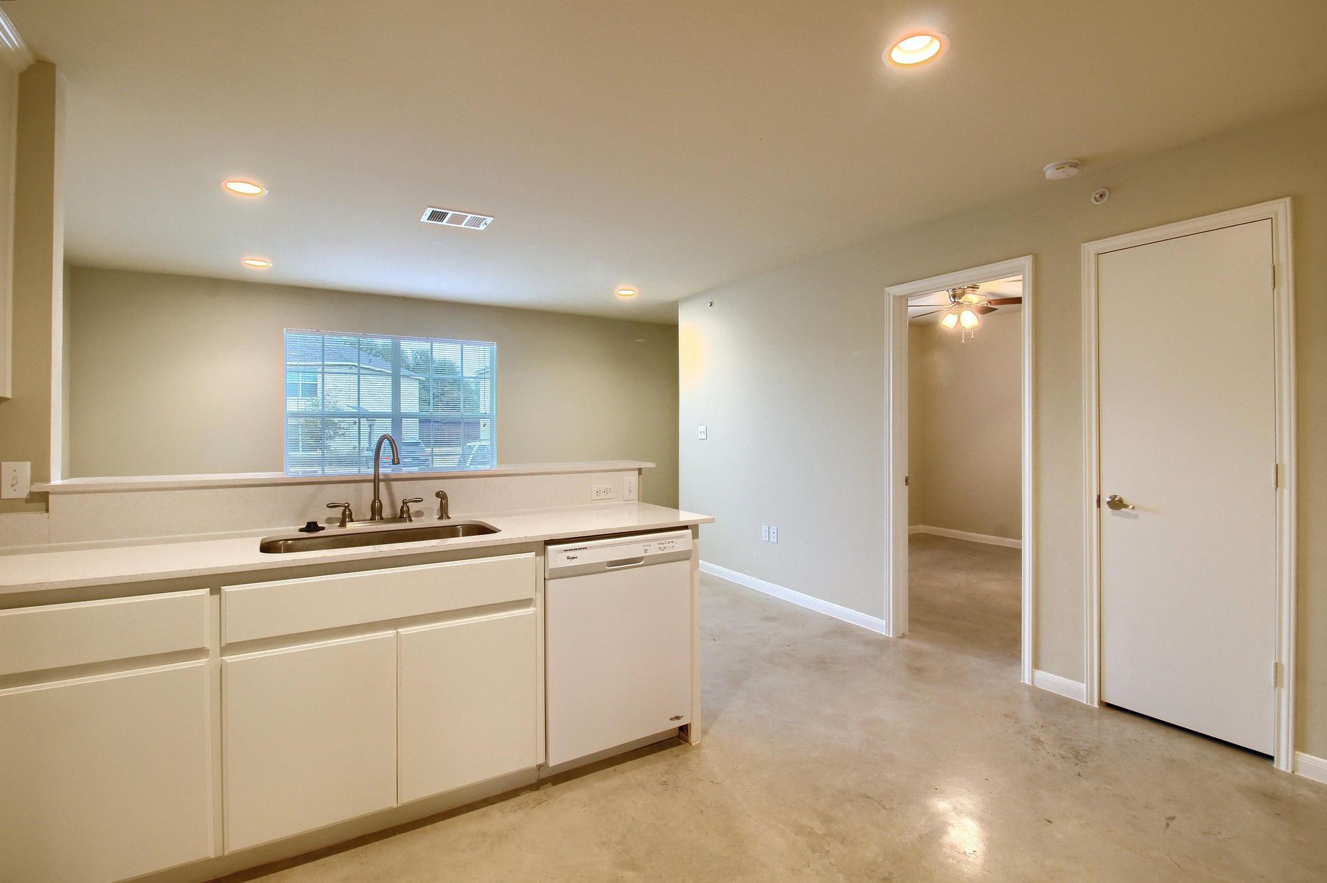 An empty kitchen with white cabinets , a sink , and a dishwasher.